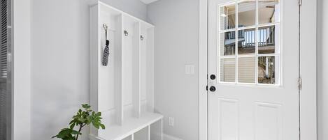 A white door with a window, a white bench, and a white wall with a vent.