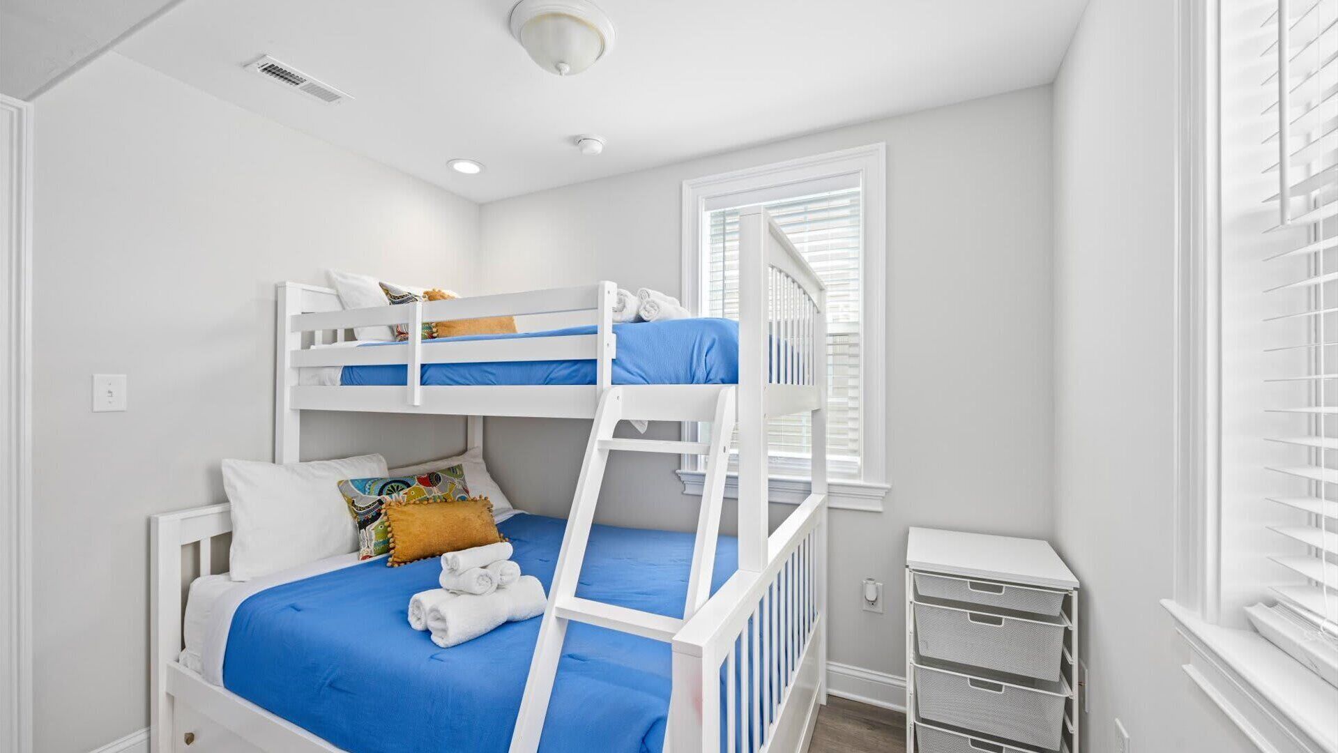 A bunk bed room with a window, a small desk, and a storage unit.