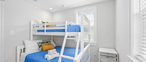 A bunk bed room with a window, a small desk, and a storage unit.
