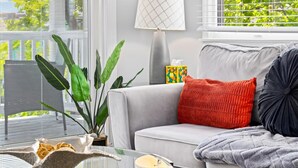 A living room with a grey sofa, a red throw pillow, a black pillow, a grey blanket, a white lamp, and a large green plant. - 2BR Beach Escape - Walk to Boardwalk & Downtown OC (Ocean City)