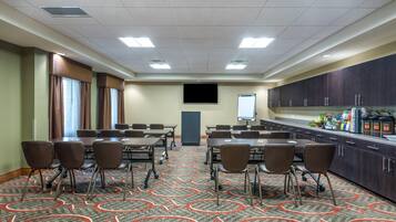 Una sala conferenze con un ampio tavolo, sedie, uno schermo per proiettore e un angolo cottura.