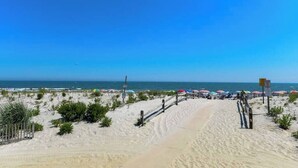 A sandy beach with umbrellas and a wooden walkway leading to the water. - Downtown OC 2BR - Walk to Beach & Boardwalk! (Ocean City)