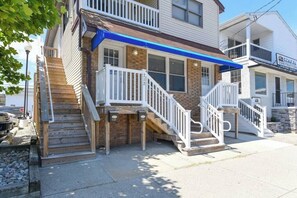 A two-story building with a wooden exterior, a blue awning, and a white front porch with a staircase. - Downtown OC 2BR - Walk to Beach & Boardwalk! (Ocean City)