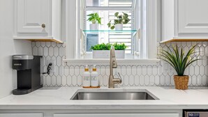 Una cocina con un grifo moderno, una cafetera Keurig y una ventana con plantas.