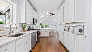 Una cocina con armarios blancos, una isla central, un ventilador de techo y vistas al comedor.