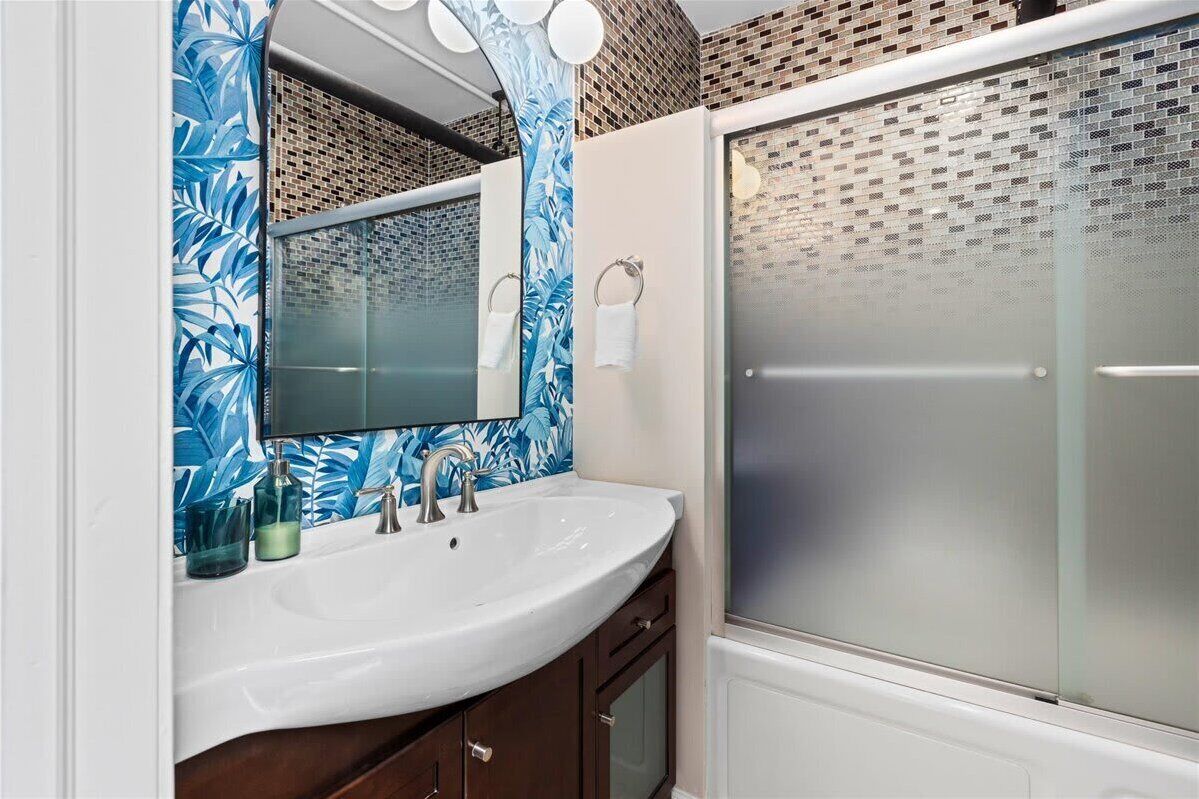 A bathroom with a white sink, a mirror, and a glass shower enclosure.