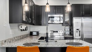 A modern kitchen with dark cabinets, stainless steel appliances, and two orange chairs. - Vibrant AC Loft w/ Beach Views, Sauna, Jacuzzi Tub (Atlantic City)