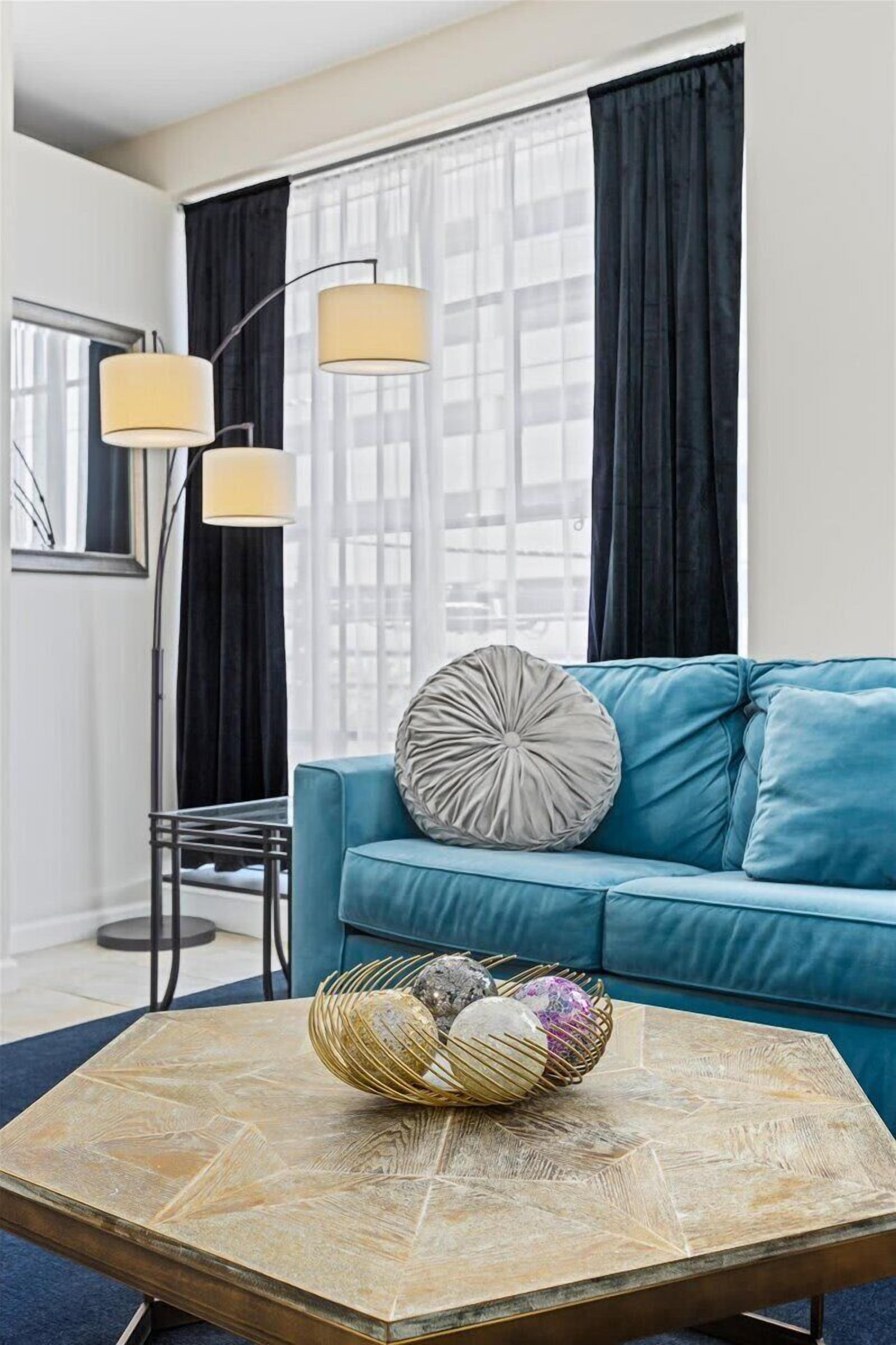 Een moderne woonkamer met een blauwe bank, een geometrisch vormige salontafel en een vloerlamp.