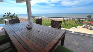A wooden table with chairs on a balcony overlooking a beach and ocean. - Villa Siempre Domingo (Tenacatita)
