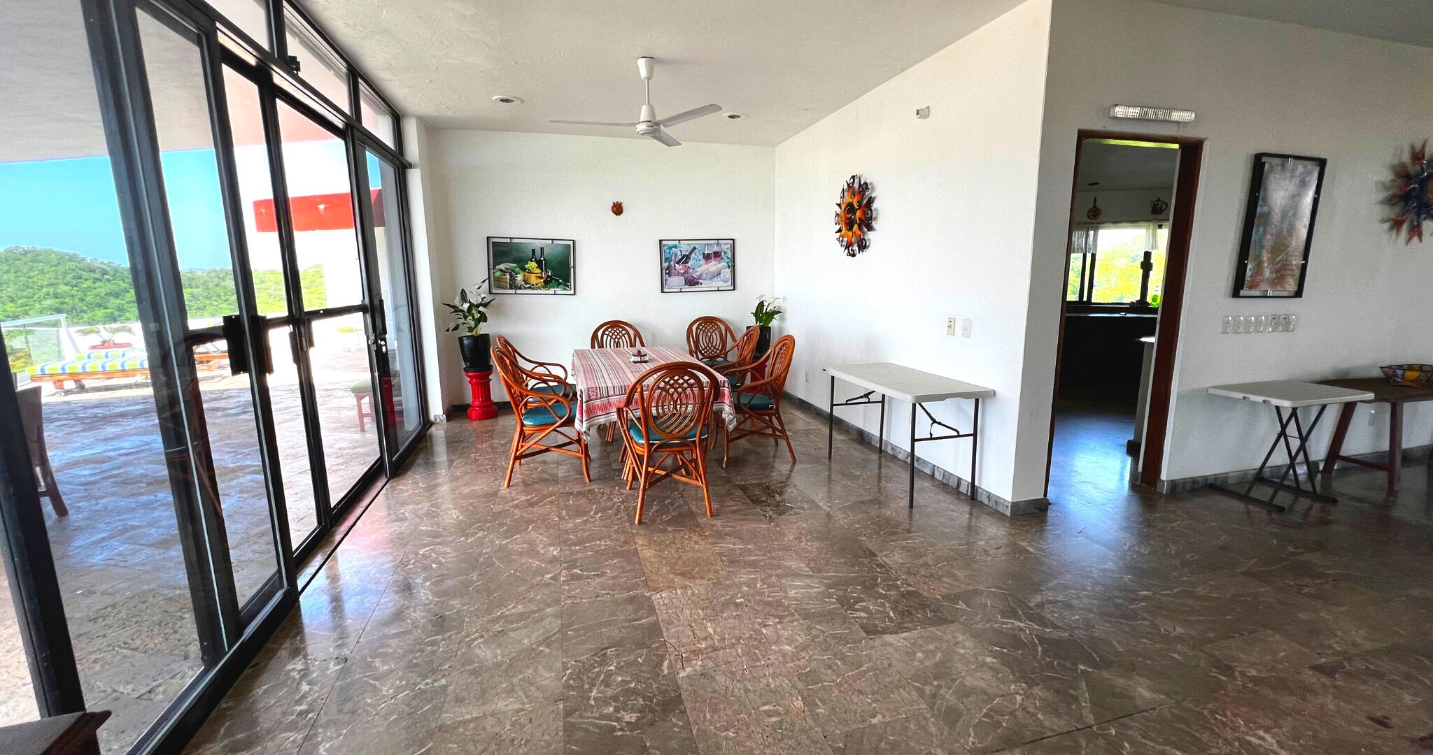 Une pièce spacieuse comprenant un coin repas avec une table et des chaises, un ventilateur de plafond et une vue dégagée grâce à de grandes fenêtres.
