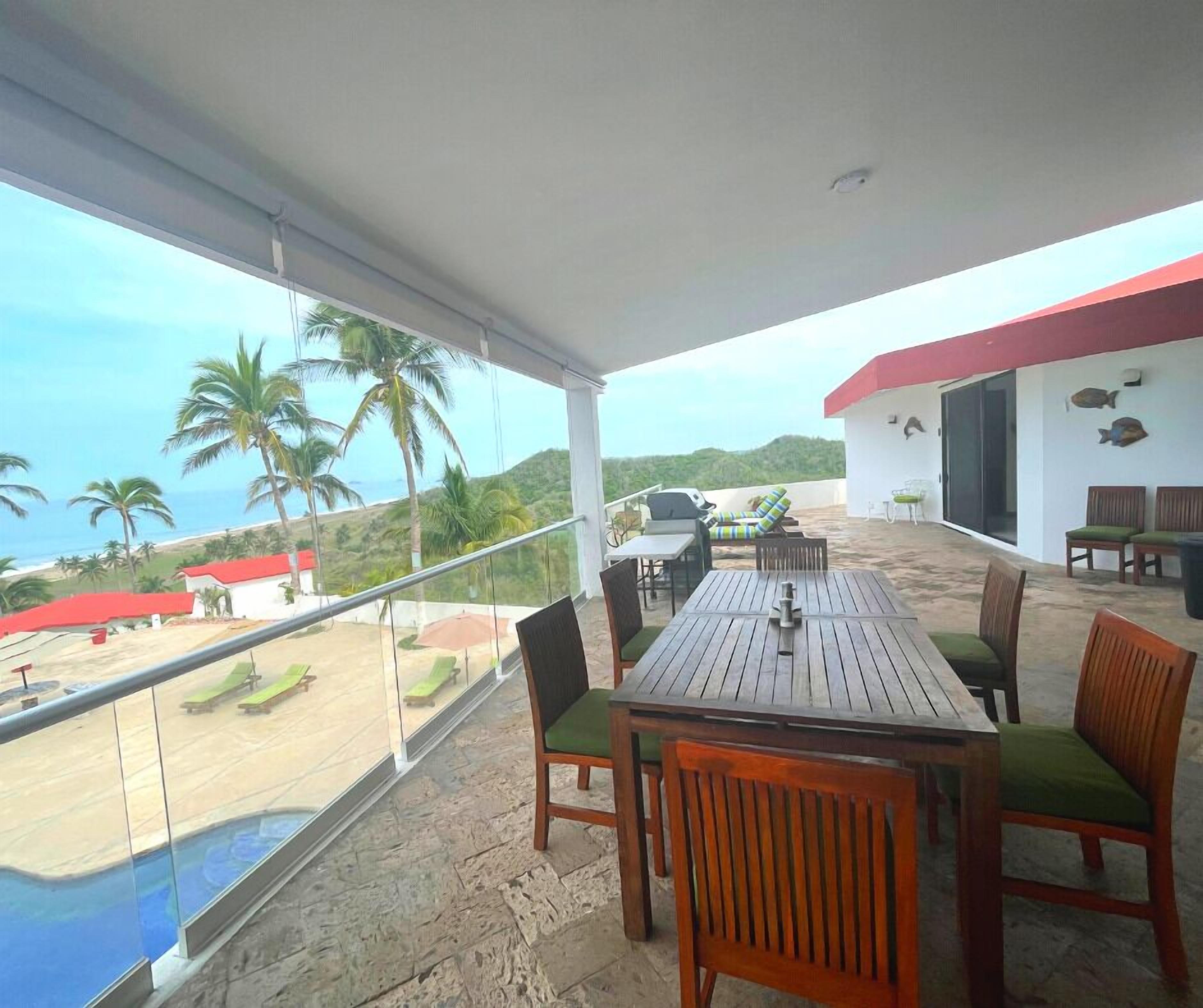 A covered outdoor dining area with a view of the beach and palm trees.