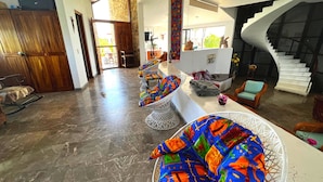 A spacious living area with a marble floor, a white curved staircase, and colorful woven chairs. - Villa Siempre Domingo (Tenacatita)