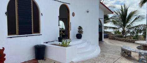 A white building with a curved roof, large windows, and a stone patio with a mosaic table.