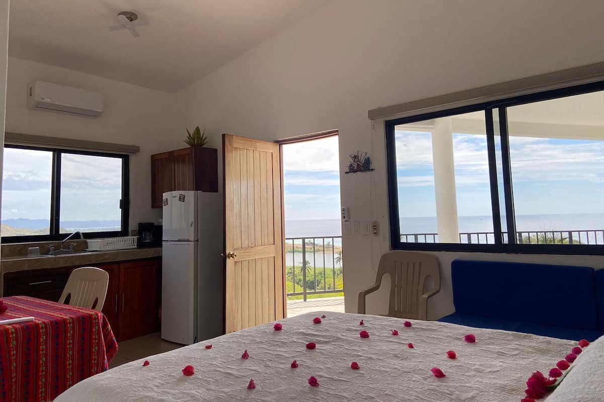 Ein Zimmer mit Bett, Esstisch, Küchenzeile und einem Balkon mit Meerblick.