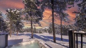 Un bain à remous installé à l’extérieur, dans un décor enneigé, avec des arbres et un coucher de soleil en arrière-plan.