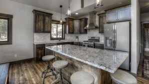 Une cuisine moderne avec des meubles en bois, un plan de travail en granit, des appareils électroménagers en acier inoxydable et des tabourets de bar.