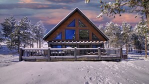 Une cabane en bois avec un toit triangulaire, de grandes fenêtres et une véranda couverte.