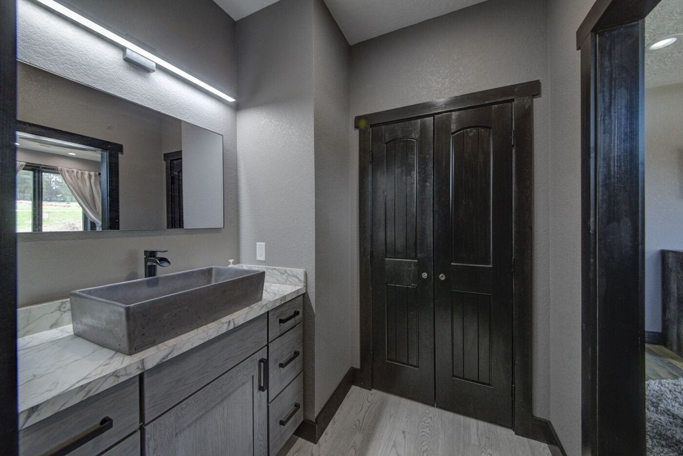 Un baño moderno con un espejo grande, un lavamanos empotrado, puertas de madera oscura y una encimera de mármol.
