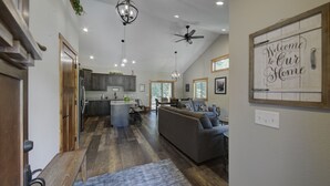 A spacious living area with a large gray sofa, a kitchen with dark cabinets, and a ceiling fan.