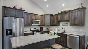 A modern kitchen with dark wood cabinets, stainless steel appliances, a granite countertop, and a bar stool.