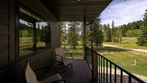 A wooden porch with two chairs and a view of a forested area.