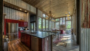 A spacious kitchen with a large island, wooden flooring, and a view of the outdoors through large windows. - Majestic Cabin near Mount Rushmore (Keystone)