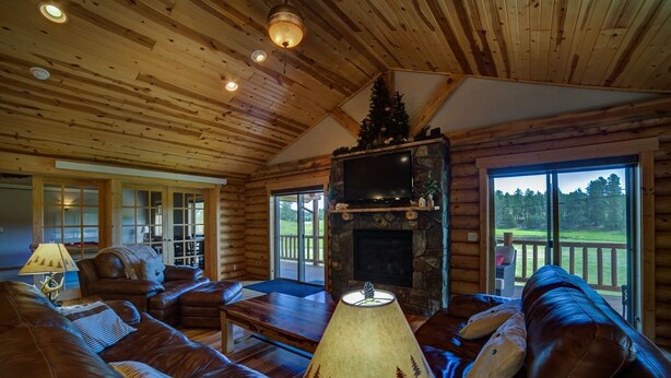 Interior de una cabaña de troncos con chimenea, sofás de cuero y televisor.