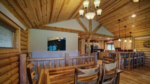 Interior rústico de una cabaña de troncos con comedor que incluye muebles de madera y una lámpara de araña.