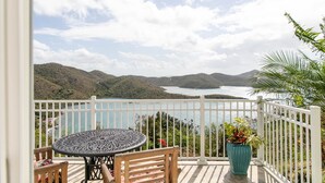 A balcony with a table and chairs, a white railing, and a view of a lake and mountains. - Sugarview Villa Cottage:  Coral Bay, Ocean View (St John)