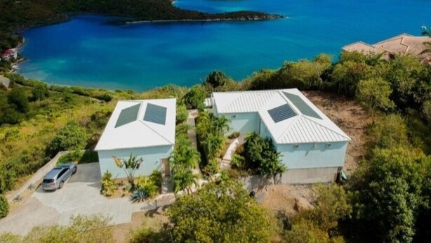 A coastal property with two light blue buildings, a parking area, and a view of the sea and hills. - Sugarview Villa Cottage:  Coral Bay, Ocean View (St John)