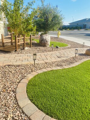 A landscaped garden area with a paved walkway, a wooden fence, a large rock, and a well-maintained lawn.