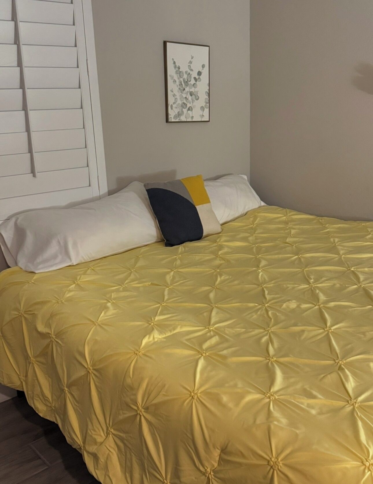 Un lit recouvert d’une courtepointe jaune à motifs, avec des oreillers blancs et un seul oreiller aux motifs jaunes et bleus.