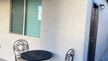 A patio with a round table and two chairs, a window with shutters, and a door with a light fixture.