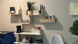 Une cuisine moderne dotée d’étagères intégrées, d’une machine à café et d’un coin repas avec une chaise blanche et une table en verre.