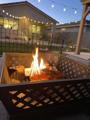 A metal fire pit with burning wood, surrounded by a lattice fence.