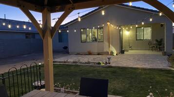 A covered patio area with string lights, a barbecue grill, and a lawn.