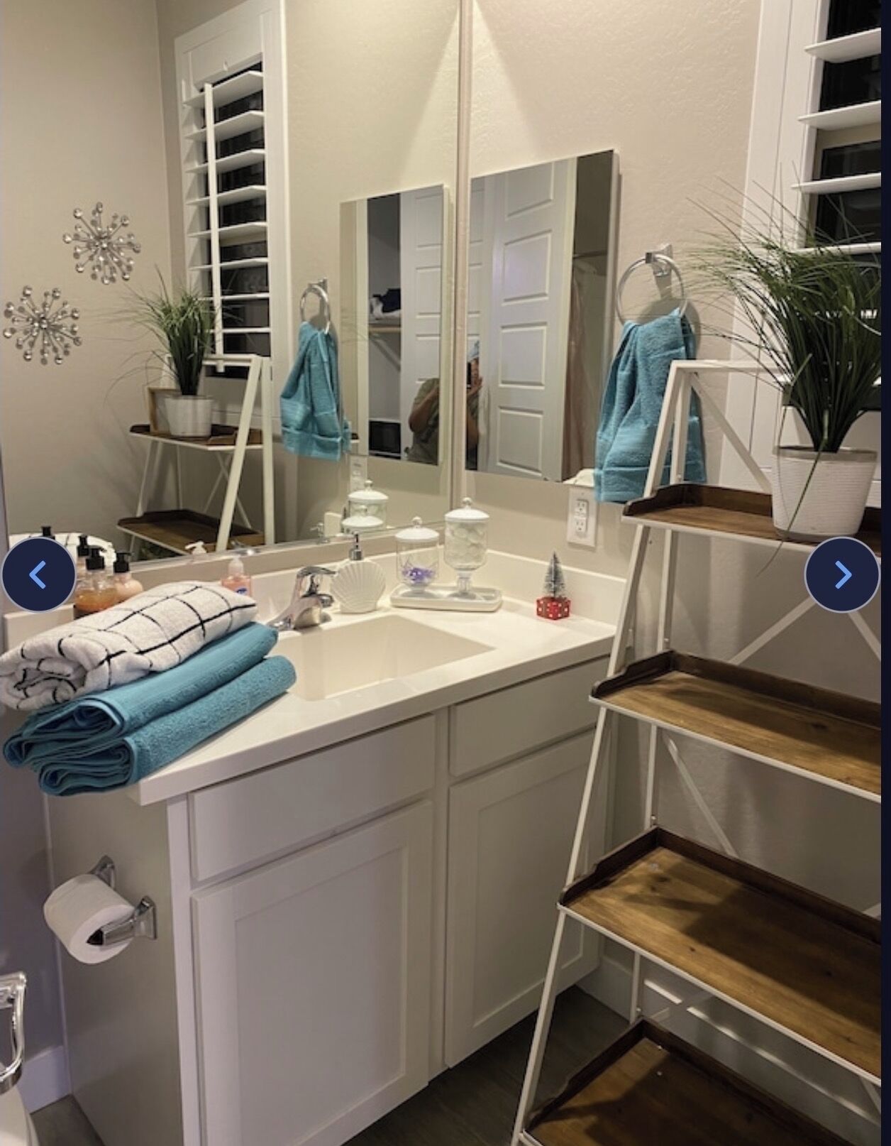 A bathroom with a white vanity, a large mirror, a sink, and a towel rack.