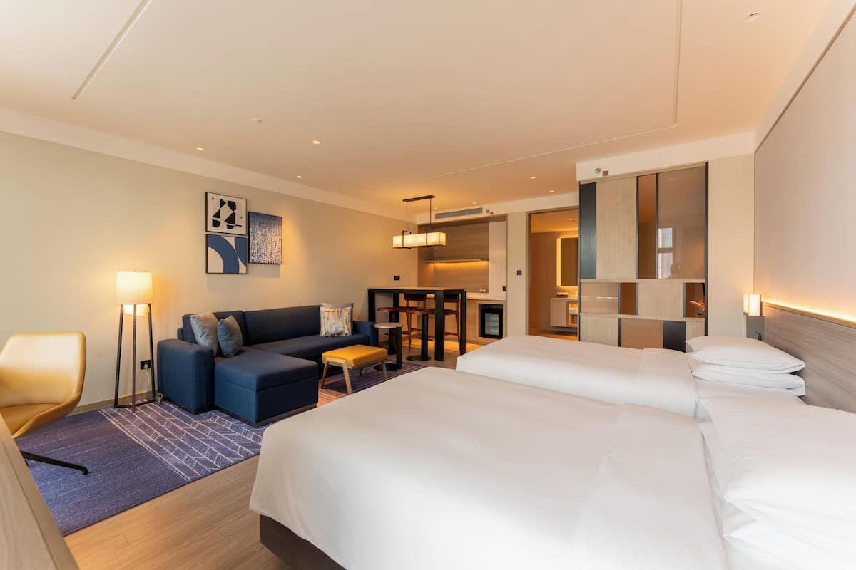 A hotel room with two beds, a sofa, a desk, and a small kitchenette.