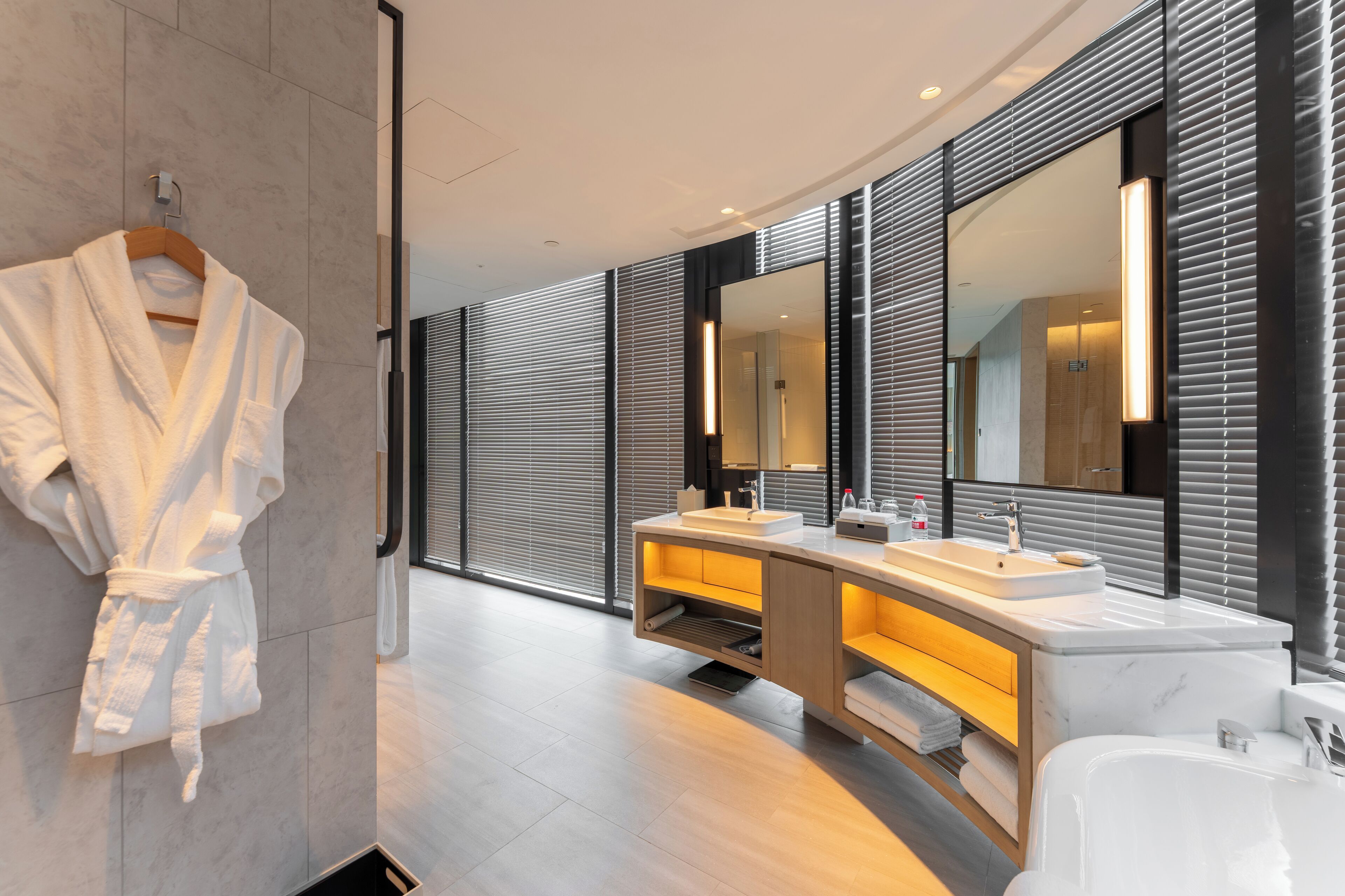A modern bathroom with a large mirror, two sinks, a bathtub, and a robe hanging on the wall.