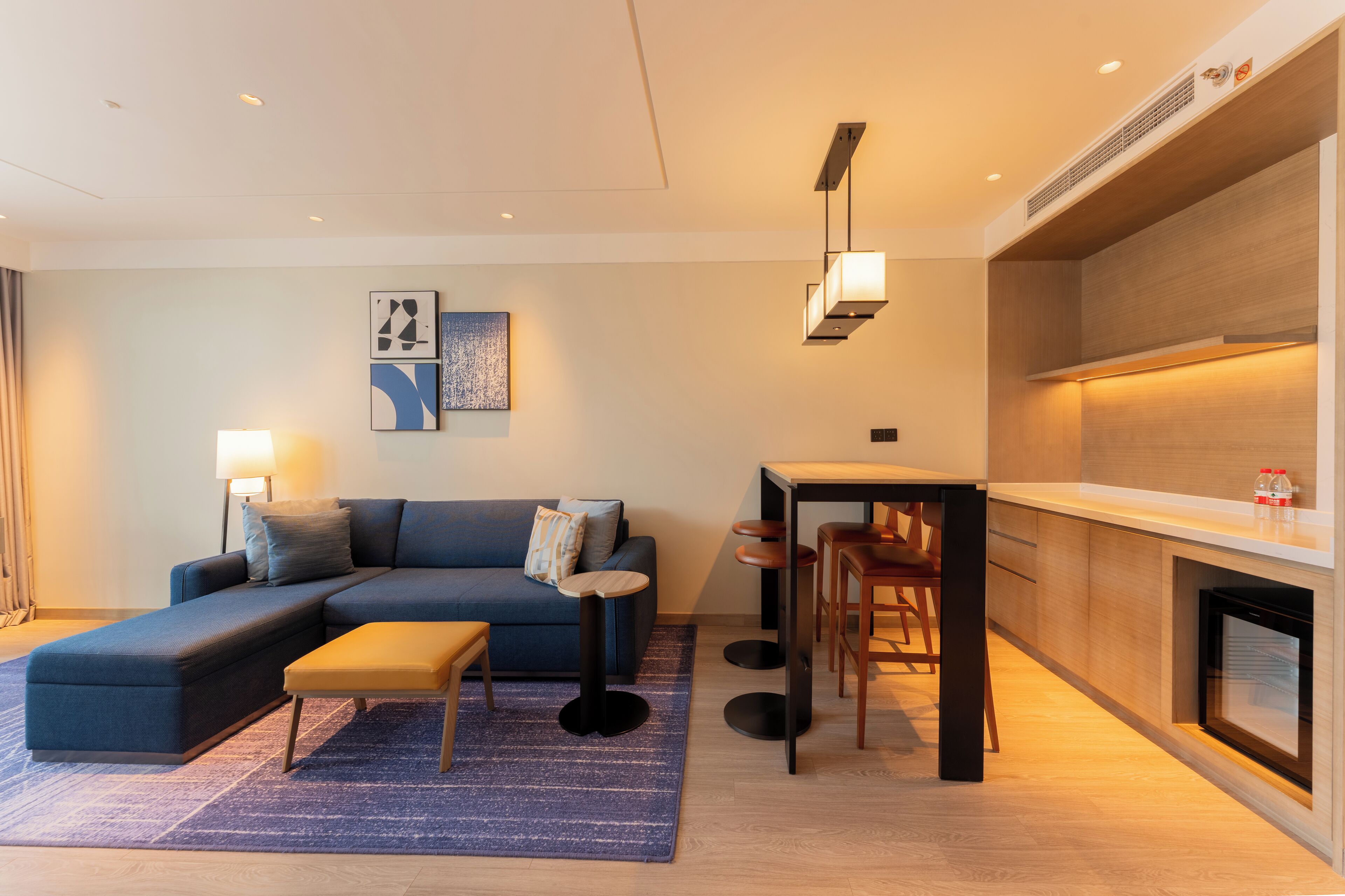 A modern living room with a sectional sofa, a small table, and bar stools.