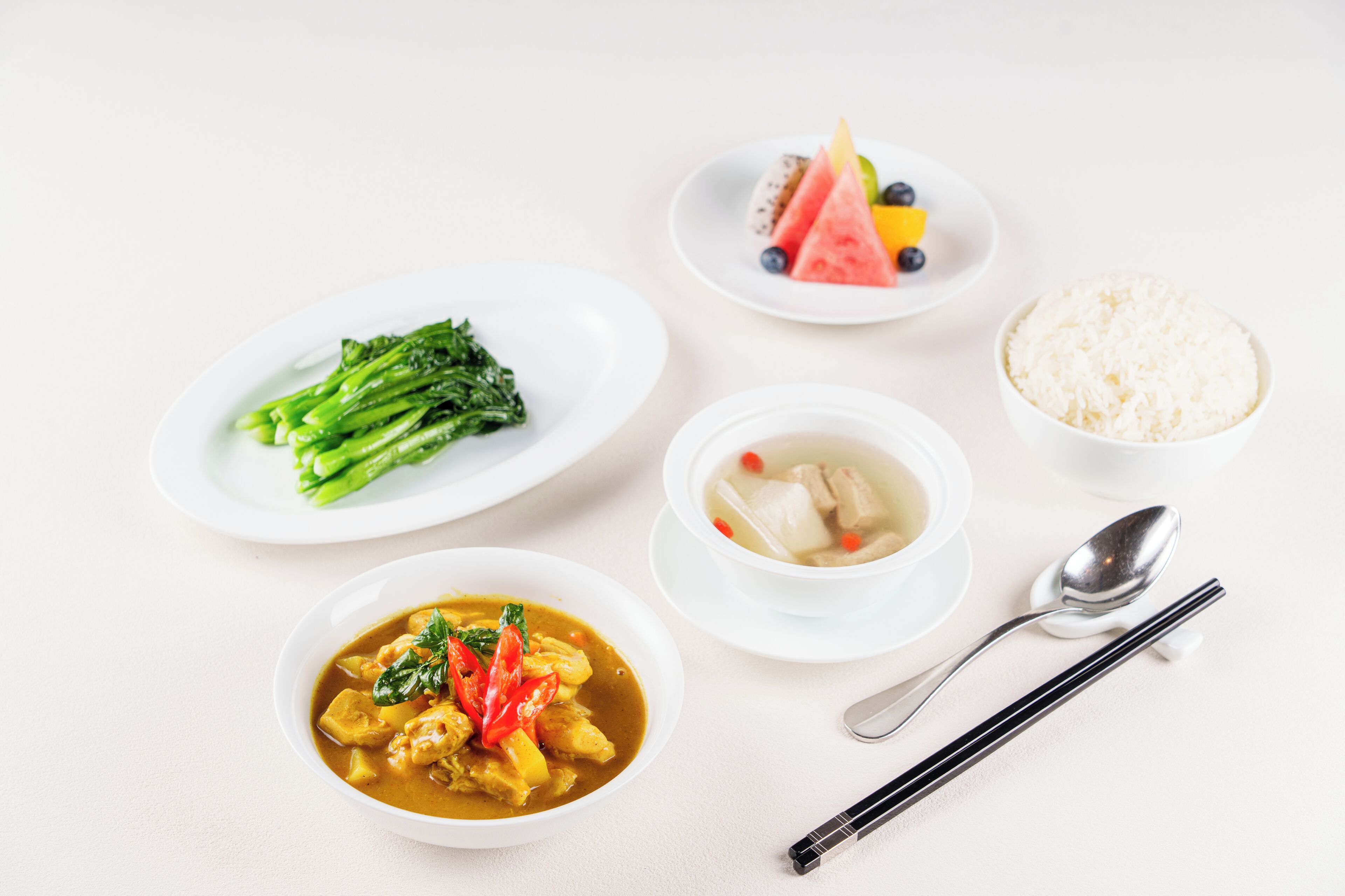 A table with various dishes including a bowl of soup, a plate of vegetables, a bowl of rice, and a plate with fruit and a dessert.