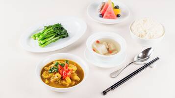 A table with various dishes including a bowl of soup, a plate of vegetables, a bowl of rice, and a plate with fruit and a dessert.
