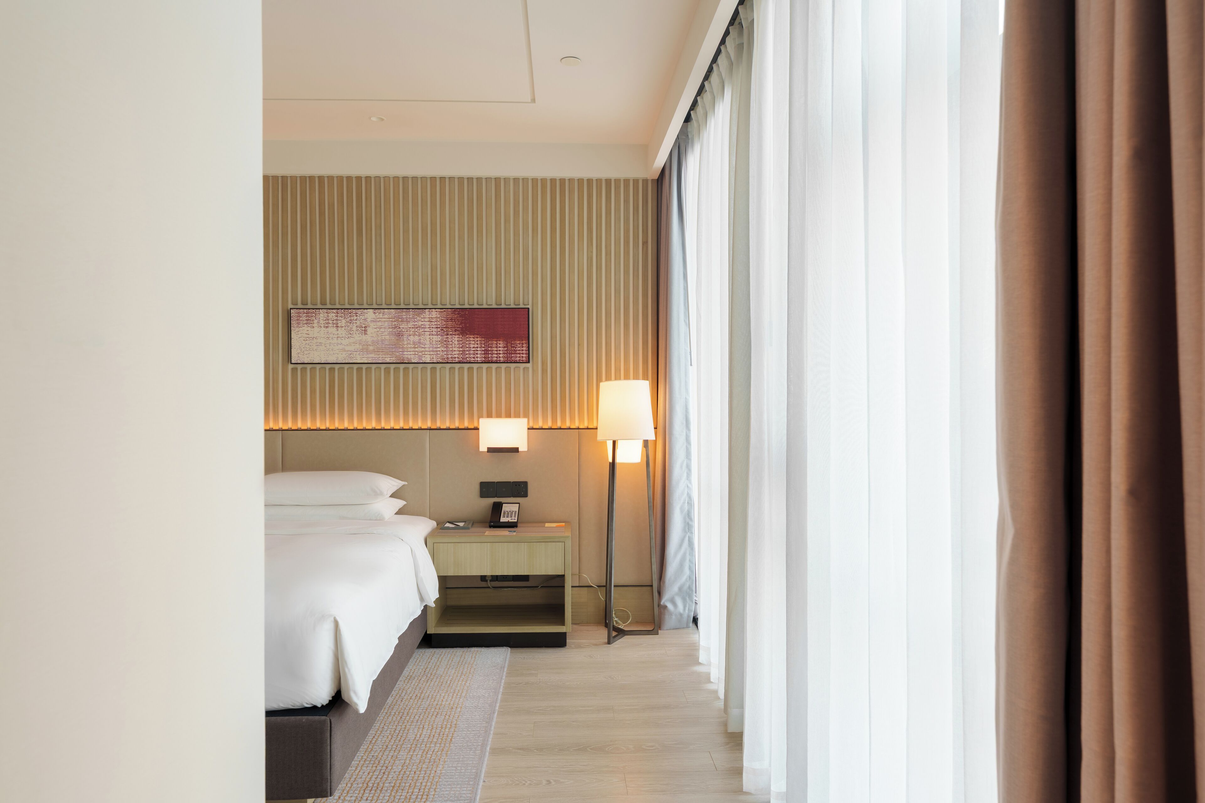 Une chambre d’hôtel avec un lit, une table de chevet, une lampe et une vue sur l’extérieur.