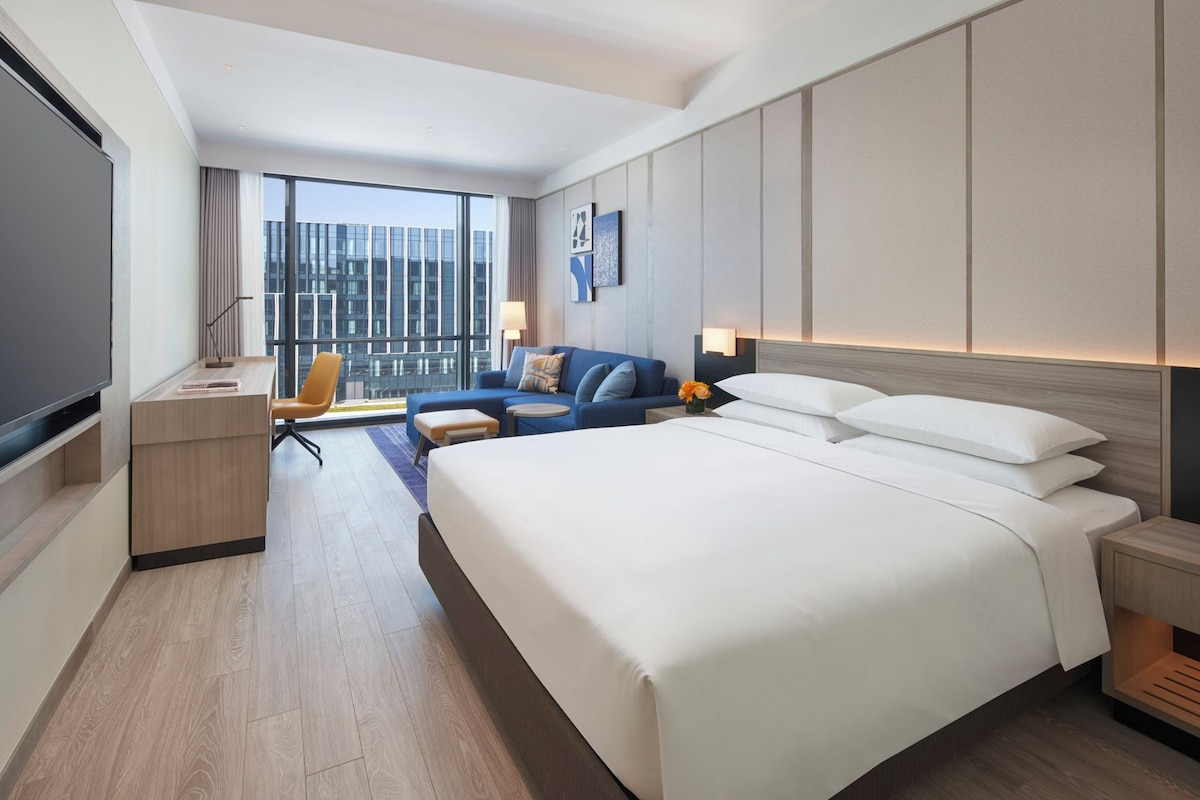 A hotel room with a large bed, a desk, a chair, and a TV.
