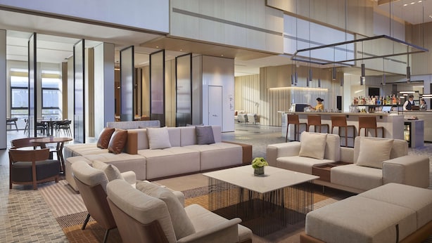 Un vestíbulo amplio con un diseño moderno, que cuenta con un gran espacio de estar con sofás y sillones, una zona de bar y vistas a la ciudad a través de amplios ventanales.