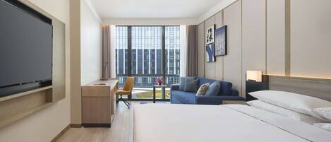 Una habitación de hotel moderna con una cama grande, un escritorio con silla, un sofá y un televisor.