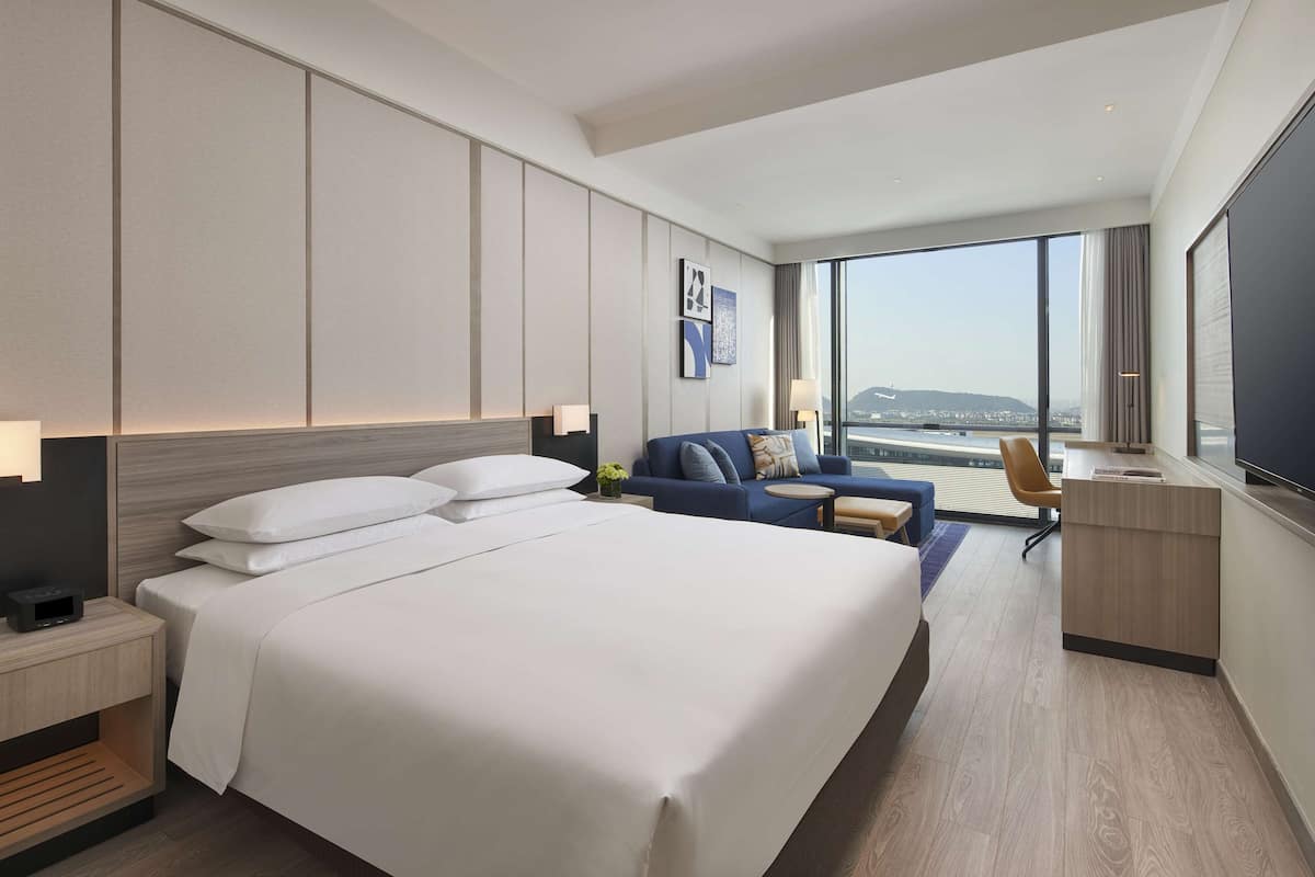 A hotel room with a large bed, a desk, a sofa, and a TV.