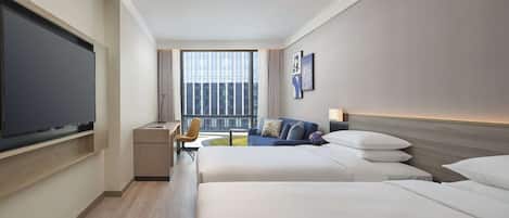 Habitación de hotel con una cama grande, otra más pequeña, un escritorio, una silla, un televisor y una ventana con vistas a la ciudad.
