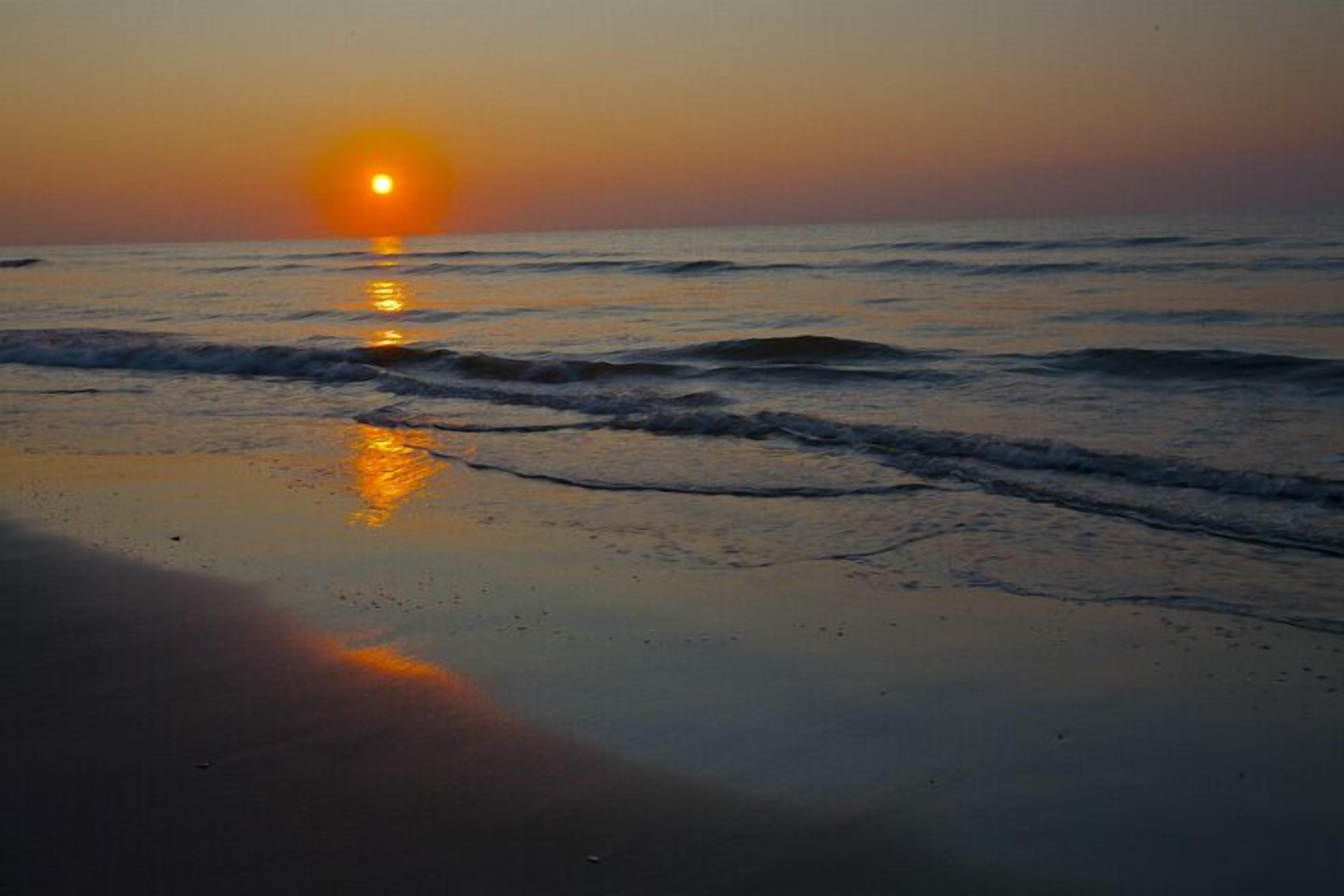 Ein Sonnenuntergang über dem Meer mit Wellen am Ufer.