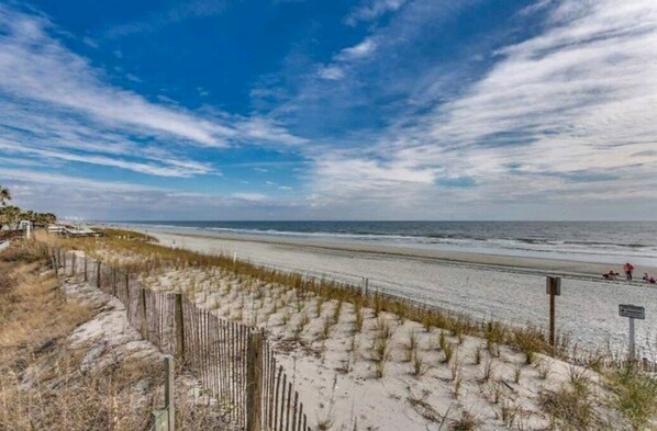 A beach with a sandy path and a wooden fence.